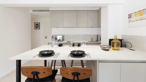 A modern kitchen with a dining table set for two, a large bottle, and a wall-mounted spice rack. - Quartier Carlton 3 rooms South with terrace (Cannes)