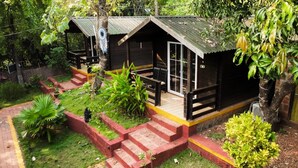 A small cabin with a porch, steps leading up to the entrance, and a garden area with various plants. - Greenland cottage (Arambol)