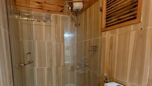 A wooden-paneled bathroom with a glass shower enclosure, a white toilet, and a wooden ceiling. - Greenland cottage (Arambol)