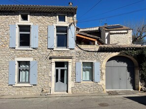 A stone building with multiple windows and shutters, a large arched entrance, and a small attached structure with a tiled roof. - Stone house with swimming pool - Gorges de l'Ardèche (Saint-Remèze)
