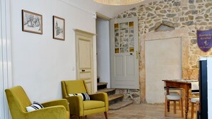 Ein Zimmer mit Steinwand, einem Holztisch, zwei gelben Sesseln, einer gewebten Deckenleuchte und einer Fußmatte.