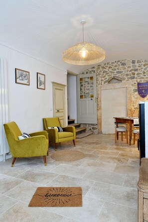 A room with a stone wall, a wooden table, two yellow armchairs, a woven ceiling light, and a welcome mat. - Stone house with swimming pool - Gorges de l'Ardèche (Saint-Remèze)