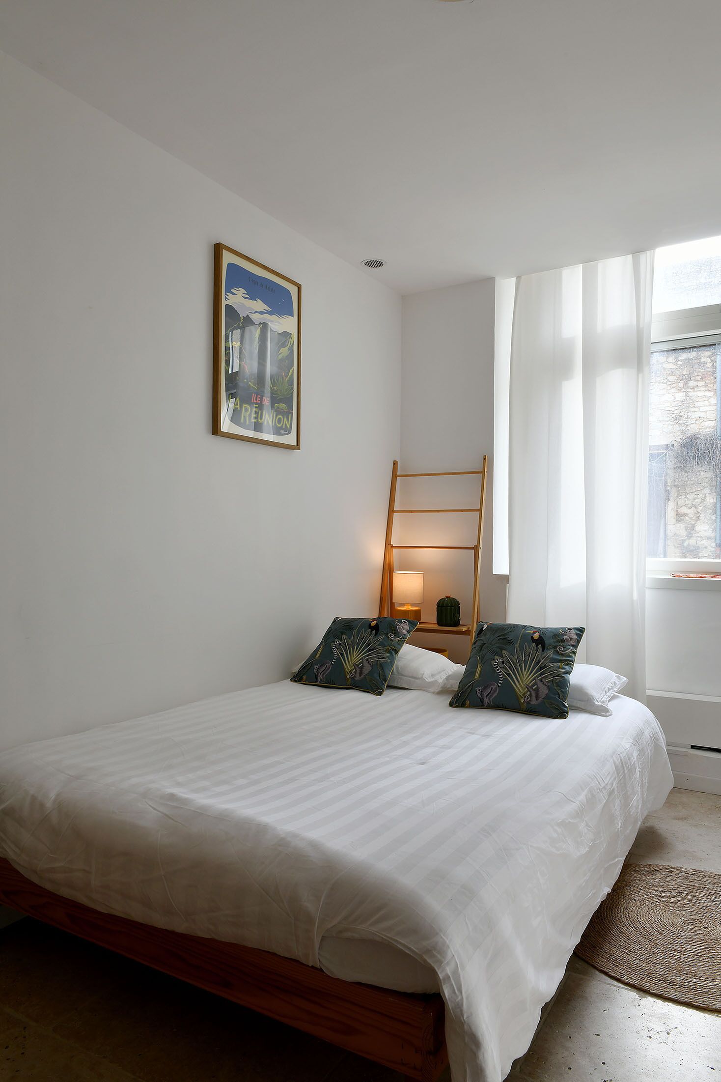 A bedroom with a bed, pillows, a ladder, a lamp, and a framed picture on the wall.