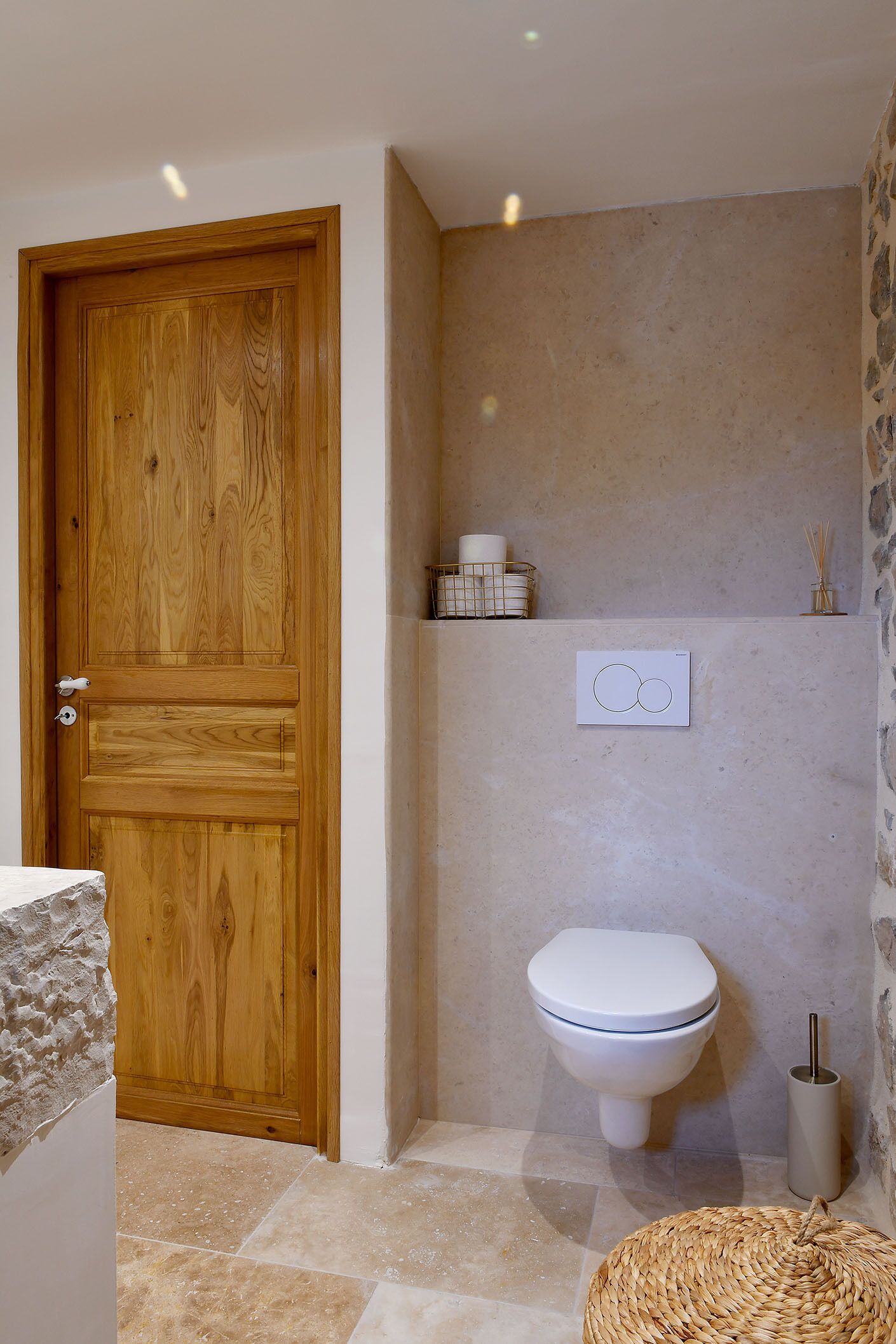 A bathroom with a wooden door, a toilet, a stone wall, and a woven basket.