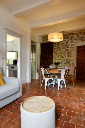 A living room with a sofa, dining table, chairs, a hanging light fixture, and a stone wall. - Stone house with swimming pool - Gorges de l'Ardèche (Saint-Remèze)