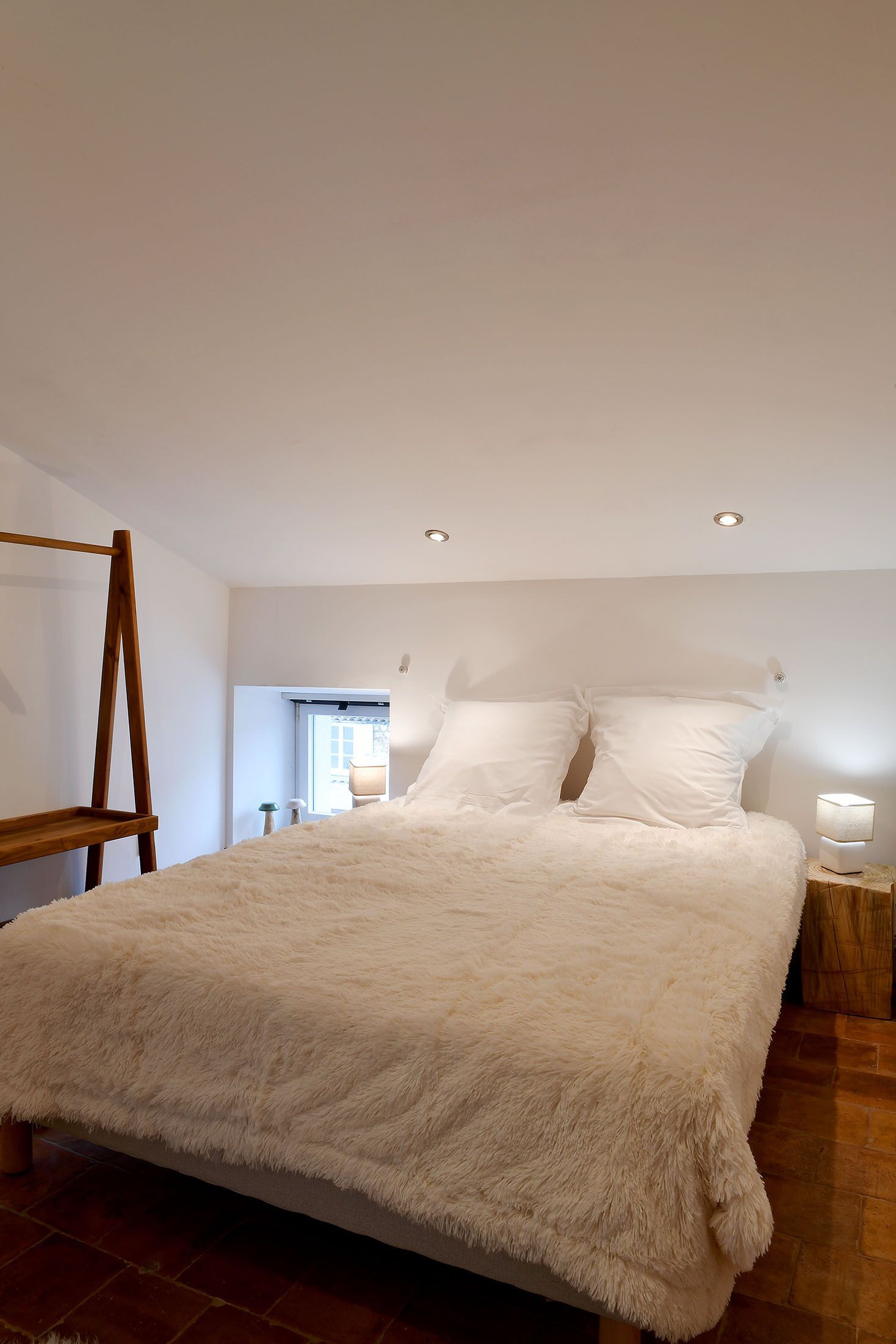 Een slaapkamer met een groot bed, een houten trap, een nachtkastje met een lamp en een raam met uitzicht.