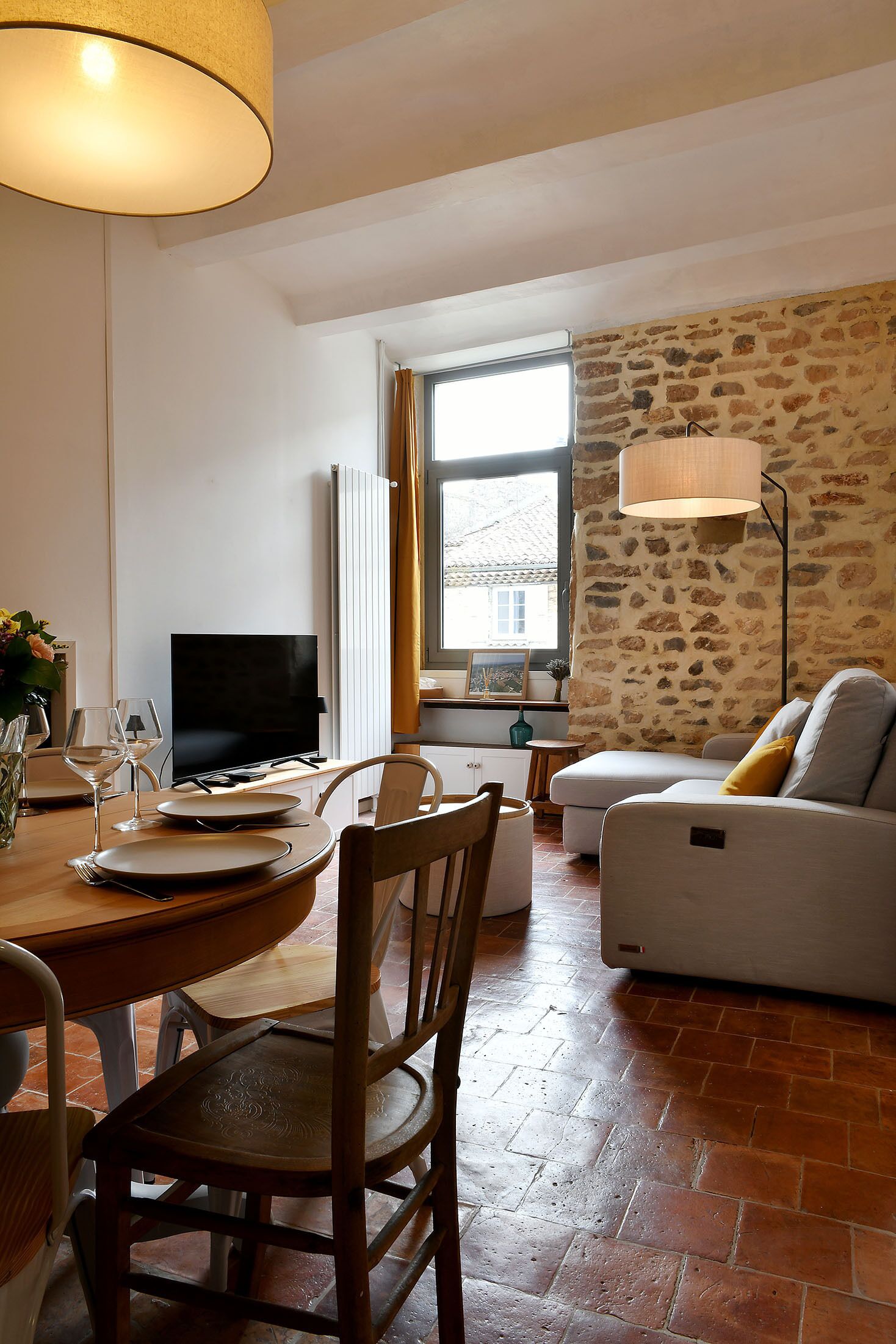 A dining area with a table set for two, a television, and a stone wall.