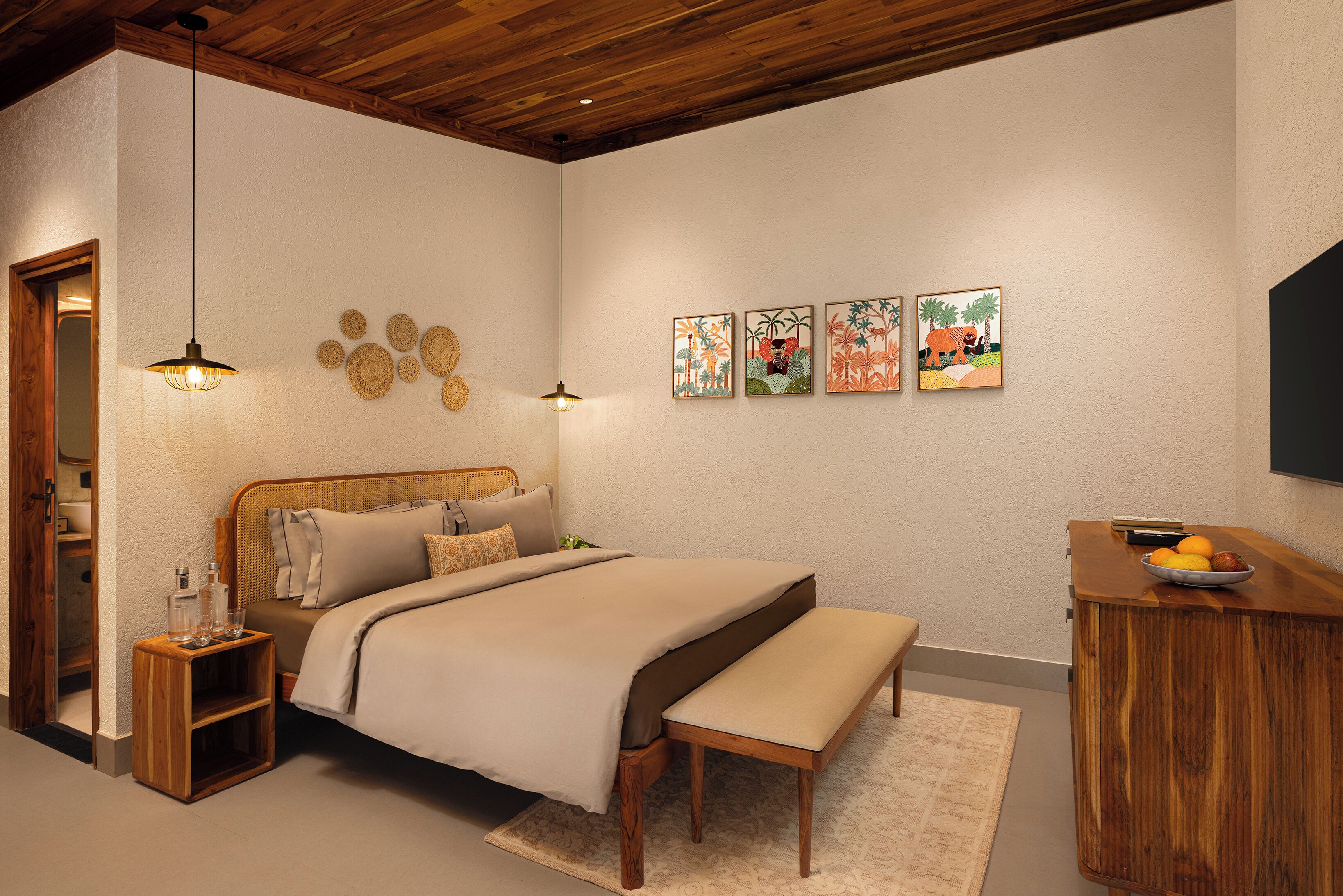 A bedroom with a wooden headboard, a bedside table with glass bottles, a bench, and wall art.