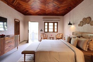 Quarto com cama grande, teto de madeira, cômoda, espelho e vista para o exterior.