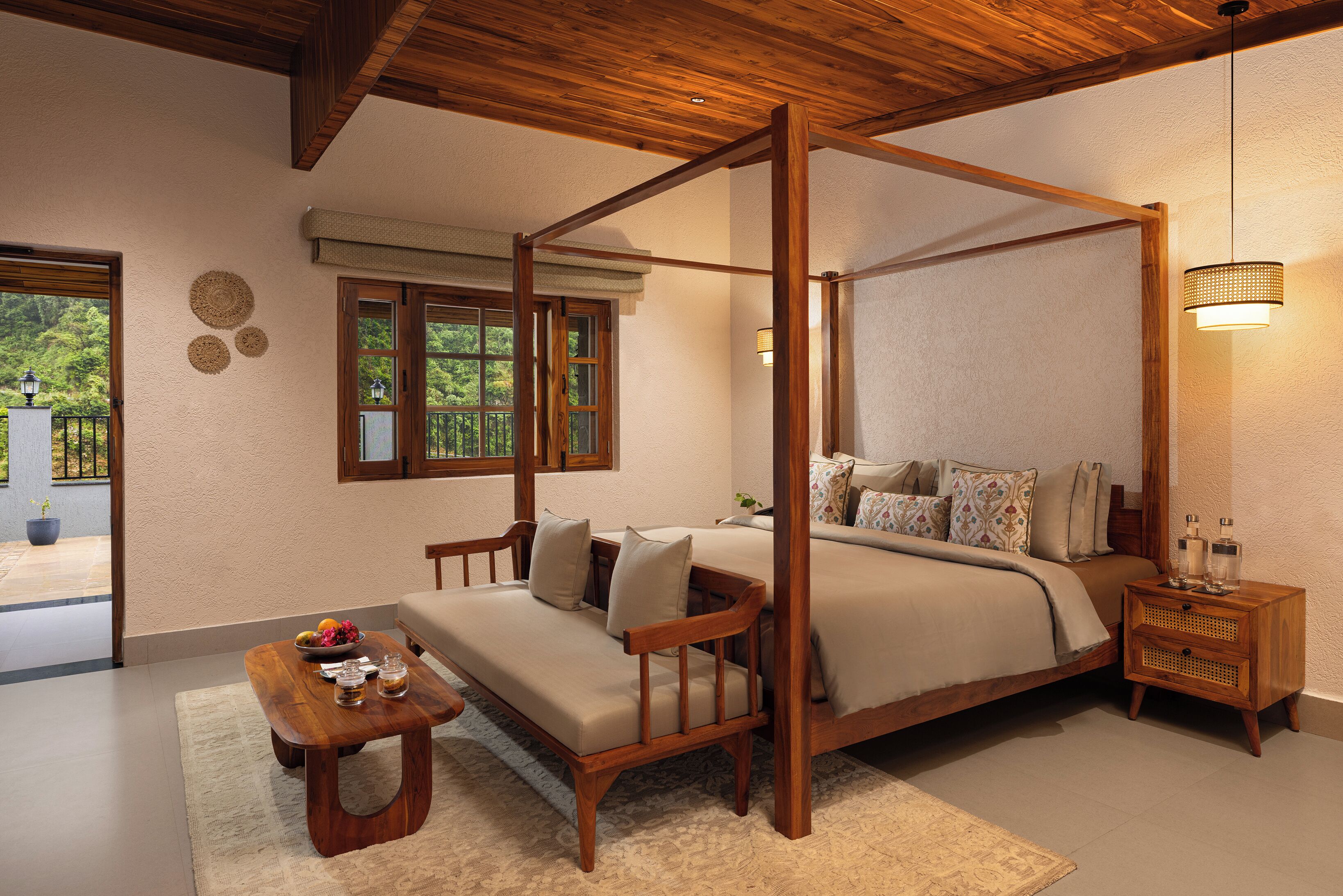 A four-poster bed with a wooden headboard, a bedside table with a lamp, and a view of the outdoors through a window.