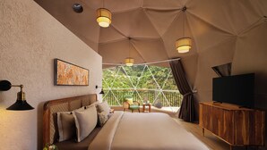 A bedroom with a large bed, a TV, a wooden cabinet, a nightstand, a lamp, a chair, and a painting. - Samsara Hill Resort By Leisure Hotels (Mussoorie,)