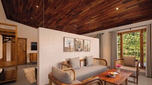 A wooden ceiling, a sofa with cushions, a dining table with a plate of fruit, and a window with a view of greenery. - Samsara Hill Resort By Leisure Hotels (Mussoorie,)