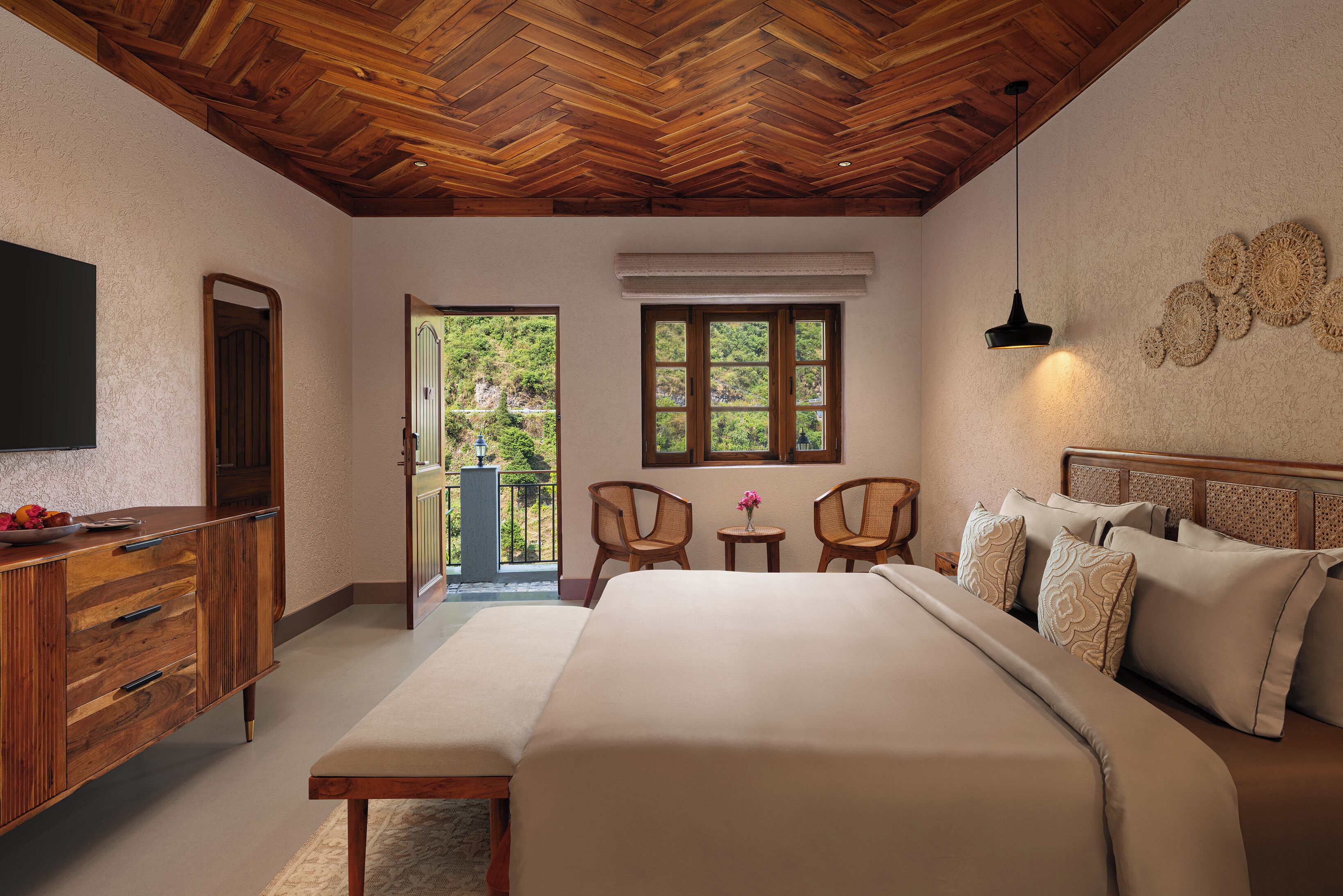 A bedroom with a large bed, wooden ceiling, a TV, a dresser, two chairs, a small table, and a balcony view.