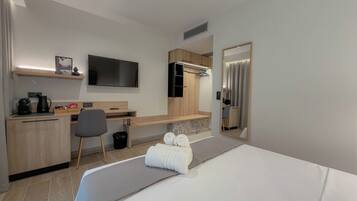 Une chambre d’hôtel comprenant un lit, un bureau, une chaise, une télévision, un miroir et une petite étagère sur laquelle est posée une photo.