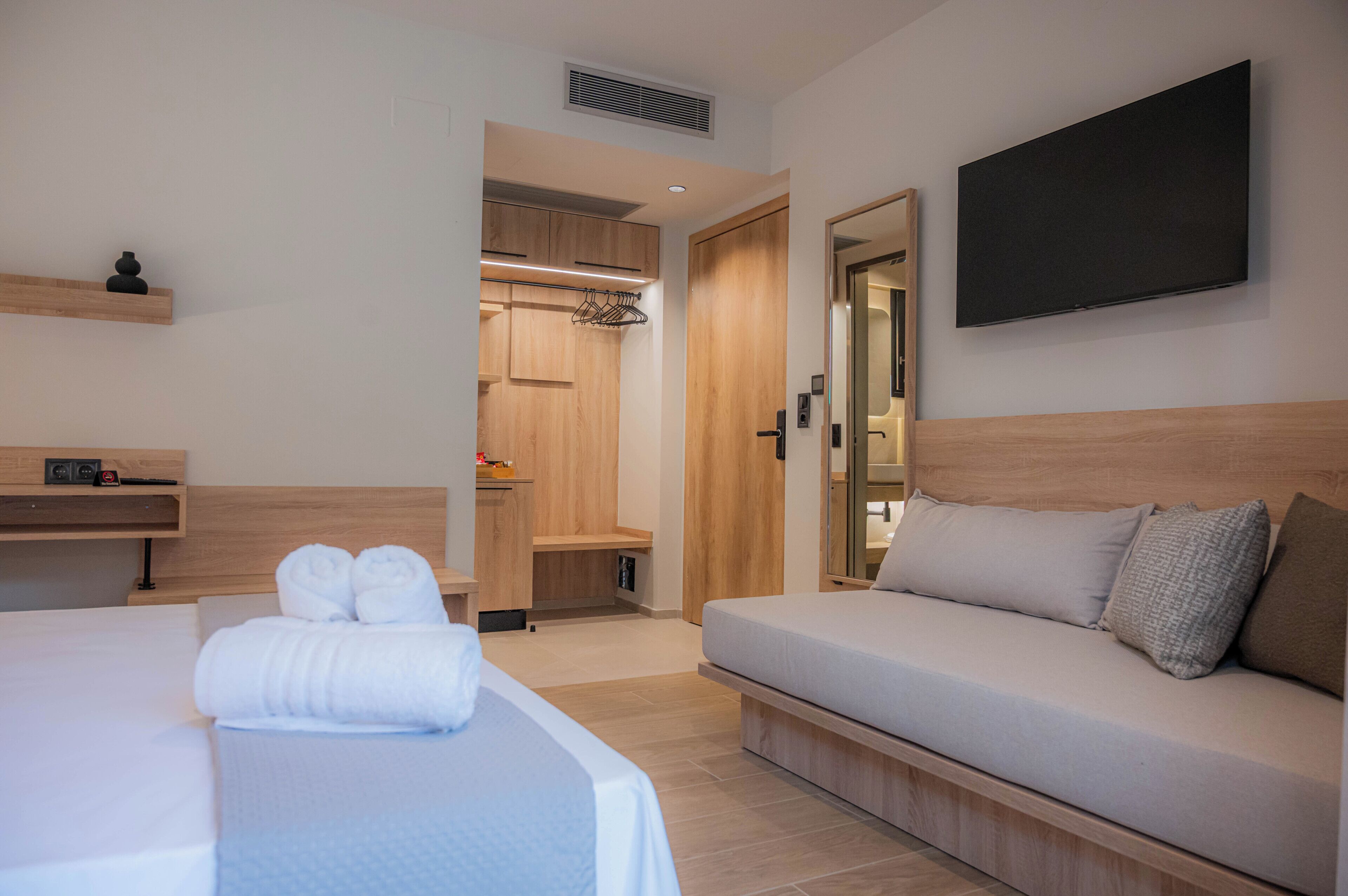 A hotel room with a bed, a sofa, a TV, a wardrobe, and a small shelf.