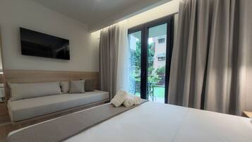 A hotel room with a bed, a sofa, a TV mounted on the wall, and a view of the outside.