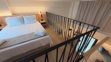 Ett modernt hotellrum med en stor säng, ett träfärgat sänggavel, ett nattduksbord, ett svart metallräcke och utsikt över staden genom fönstret.