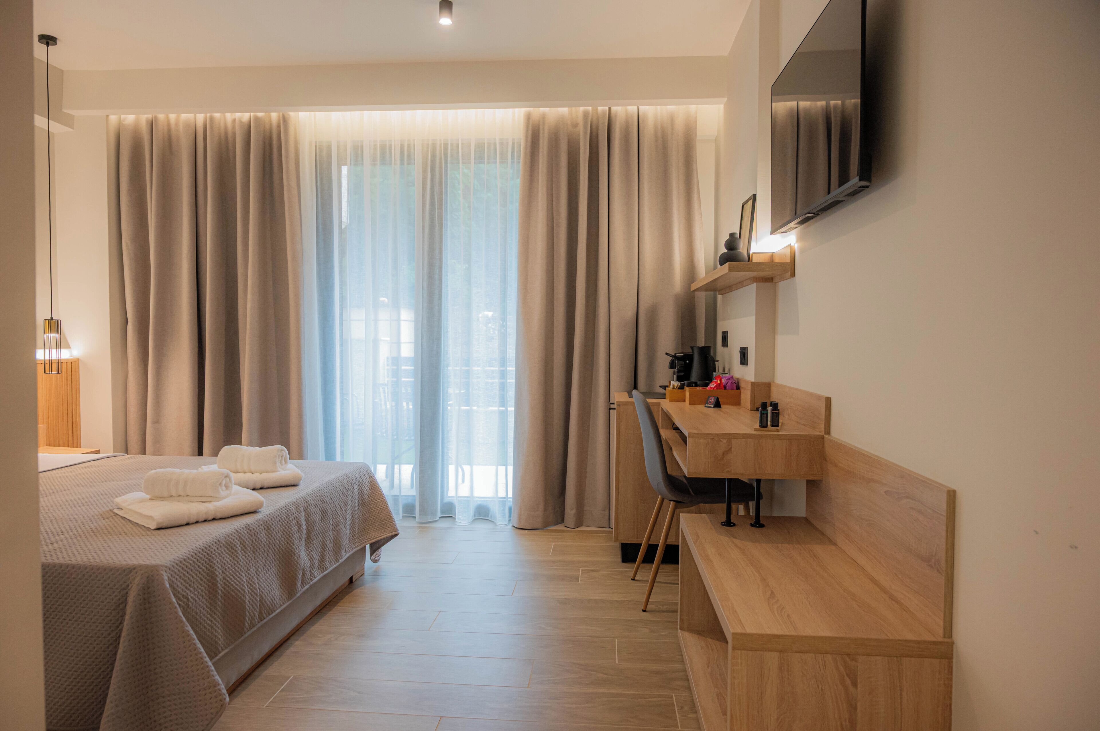 A hotel room with a bed, a desk, a chair, a TV, and a window with curtains.