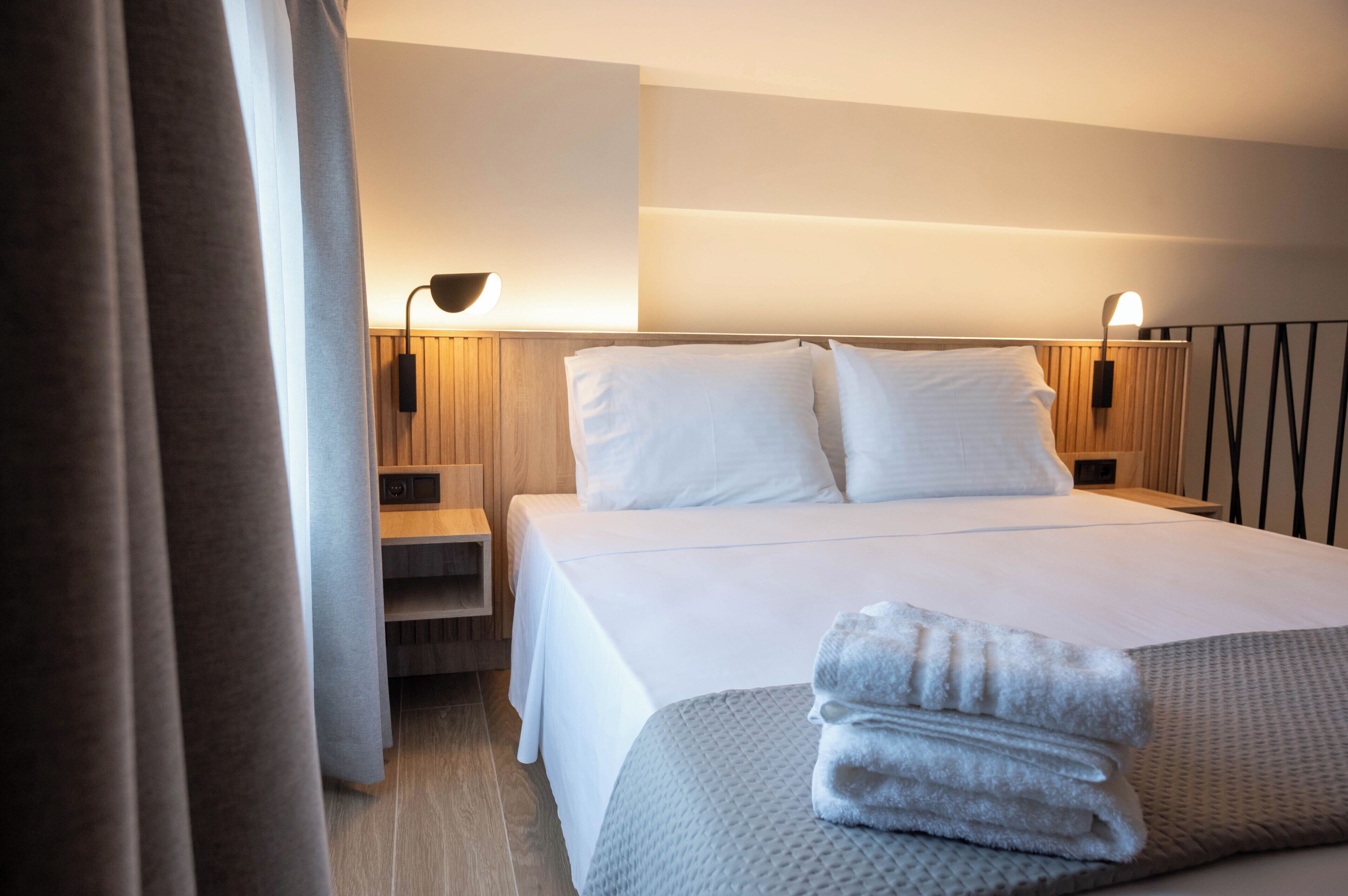 A hotel room with a bed, bedside lamps, a nightstand, and a neatly folded towel on the bed.