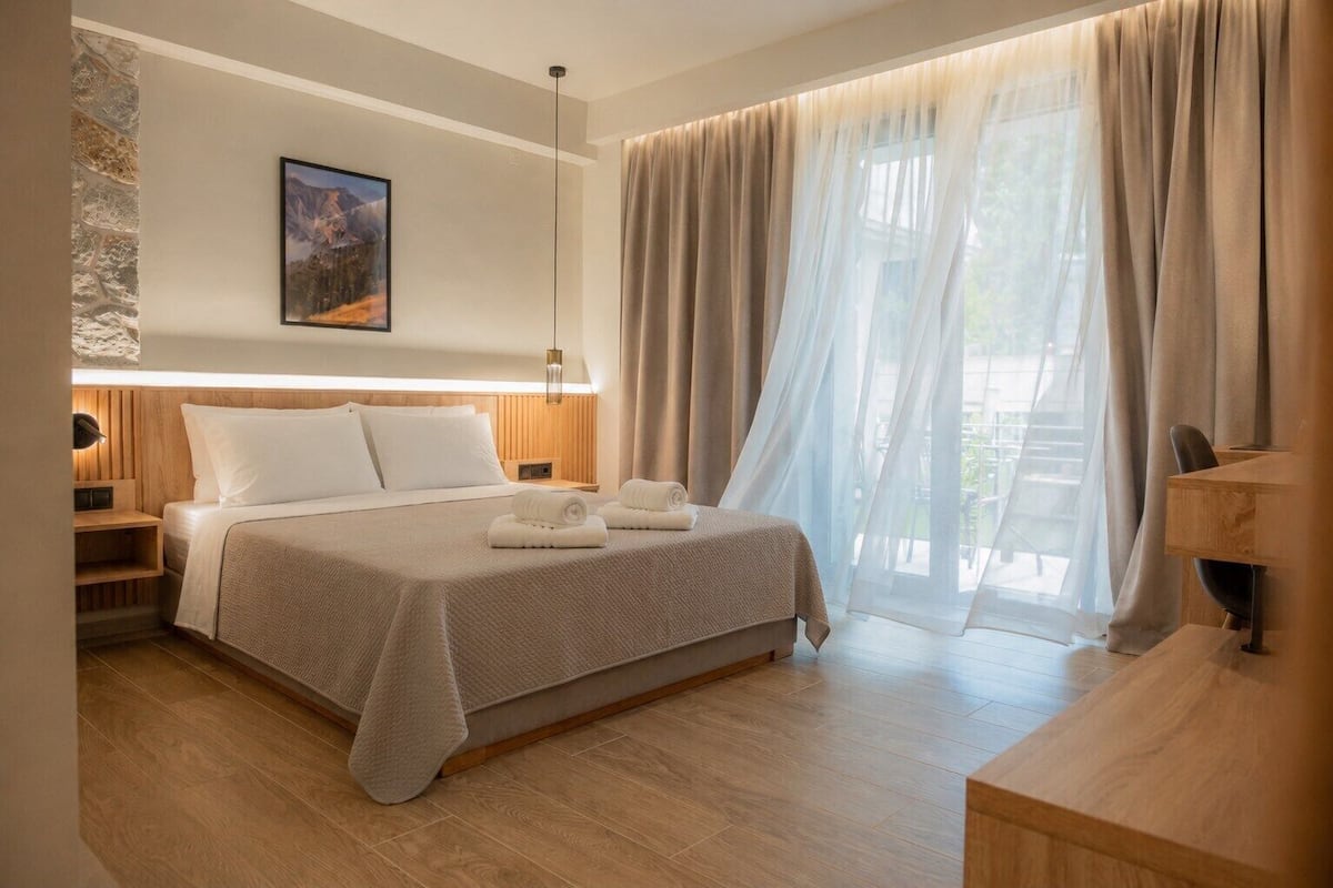 A hotel room with a bed, a nightstand, a desk, a chair, and a window with curtains.