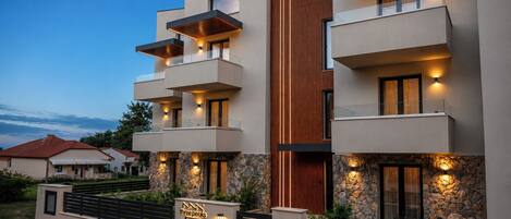 Un moderno edificio residencial de varios pisos con balcones, detalles de piedra y una entrada con portón.