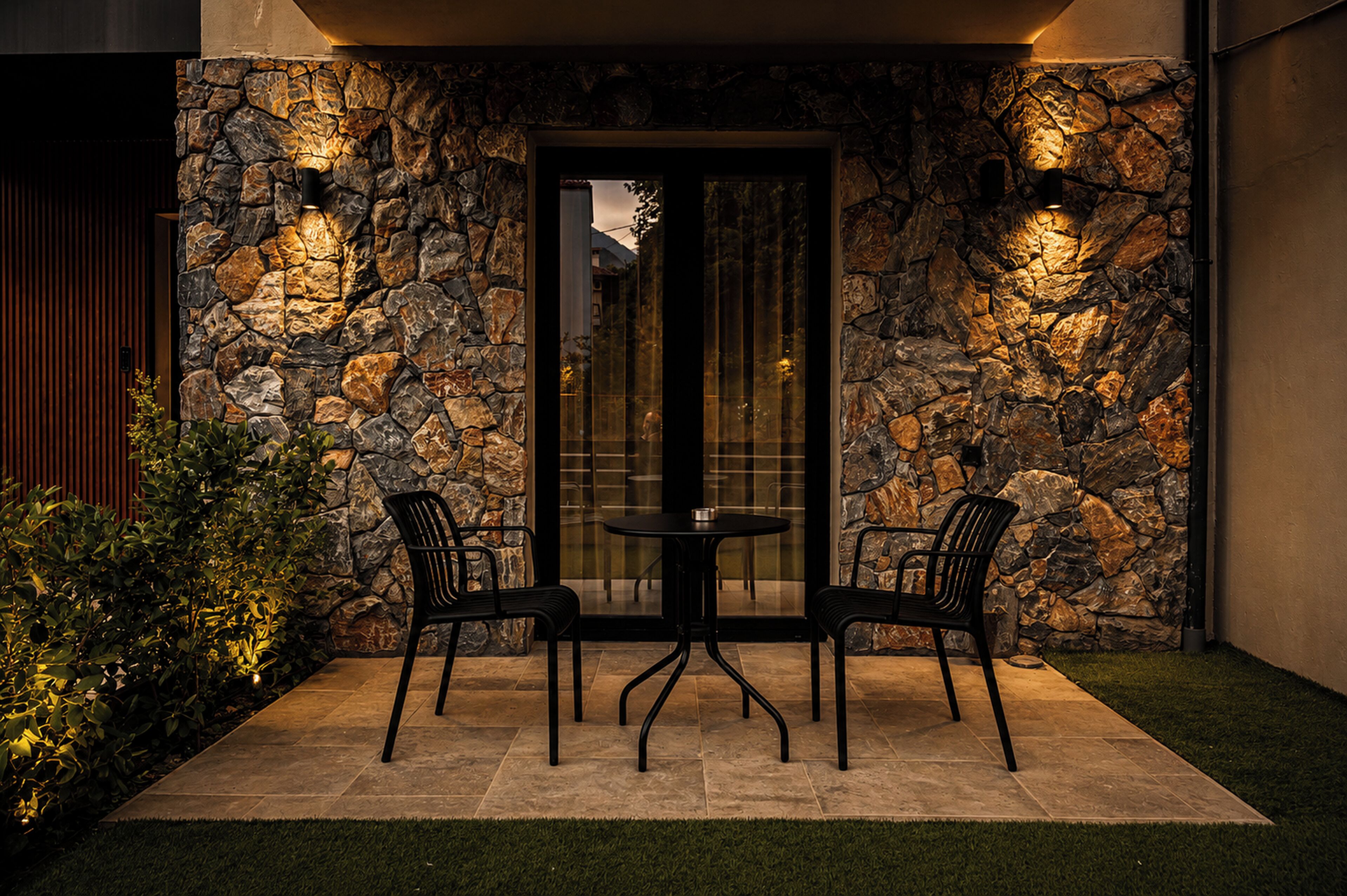 A patio with stone walls, a glass door, and two chairs.