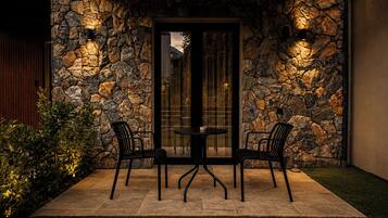 A patio with stone walls, a glass door, and two chairs.