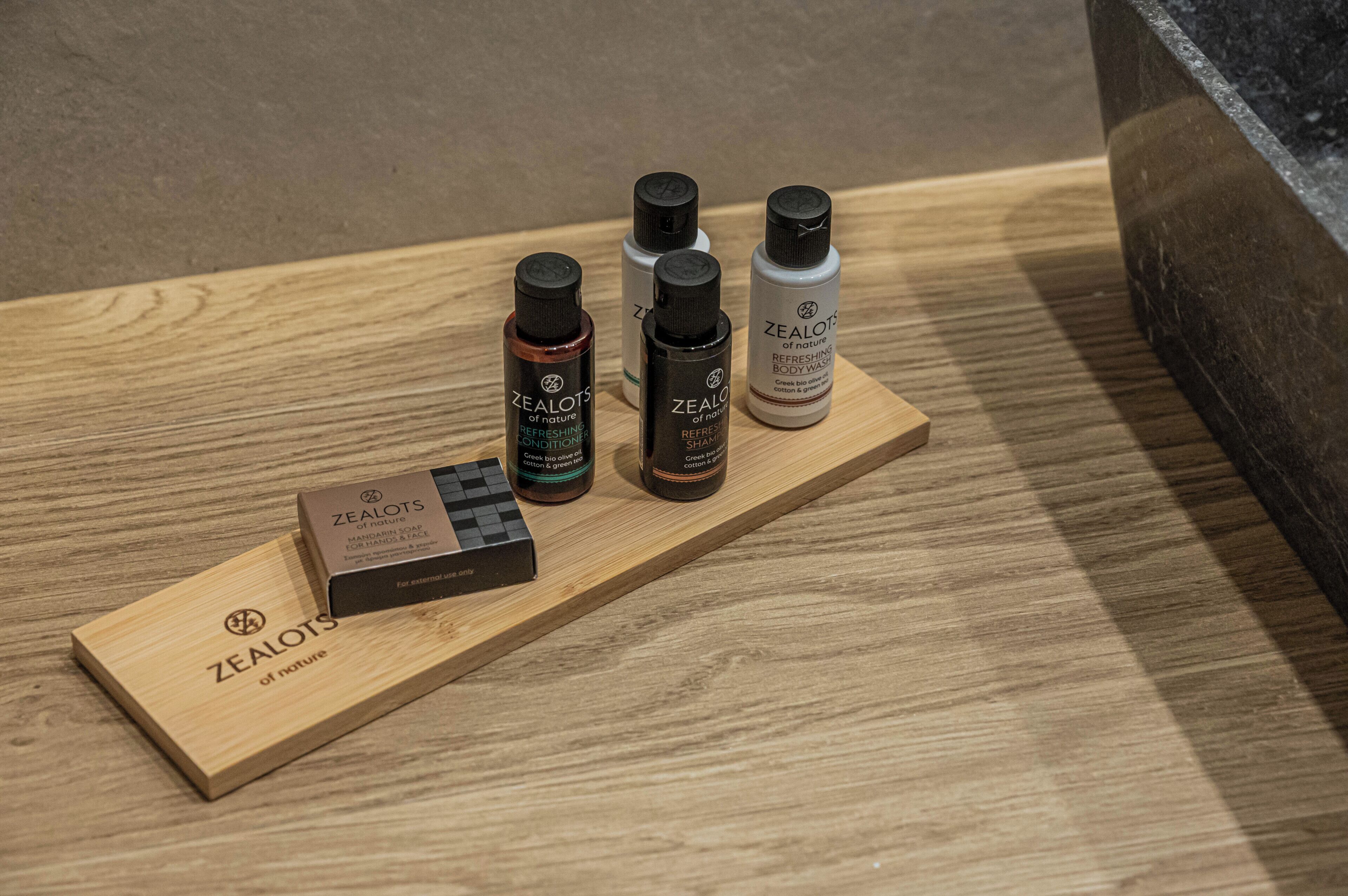 Una bandeja de madera con cuatro botellas de jabón corporal Zealots y una caja de la misma marca sobre una superficie de madera.