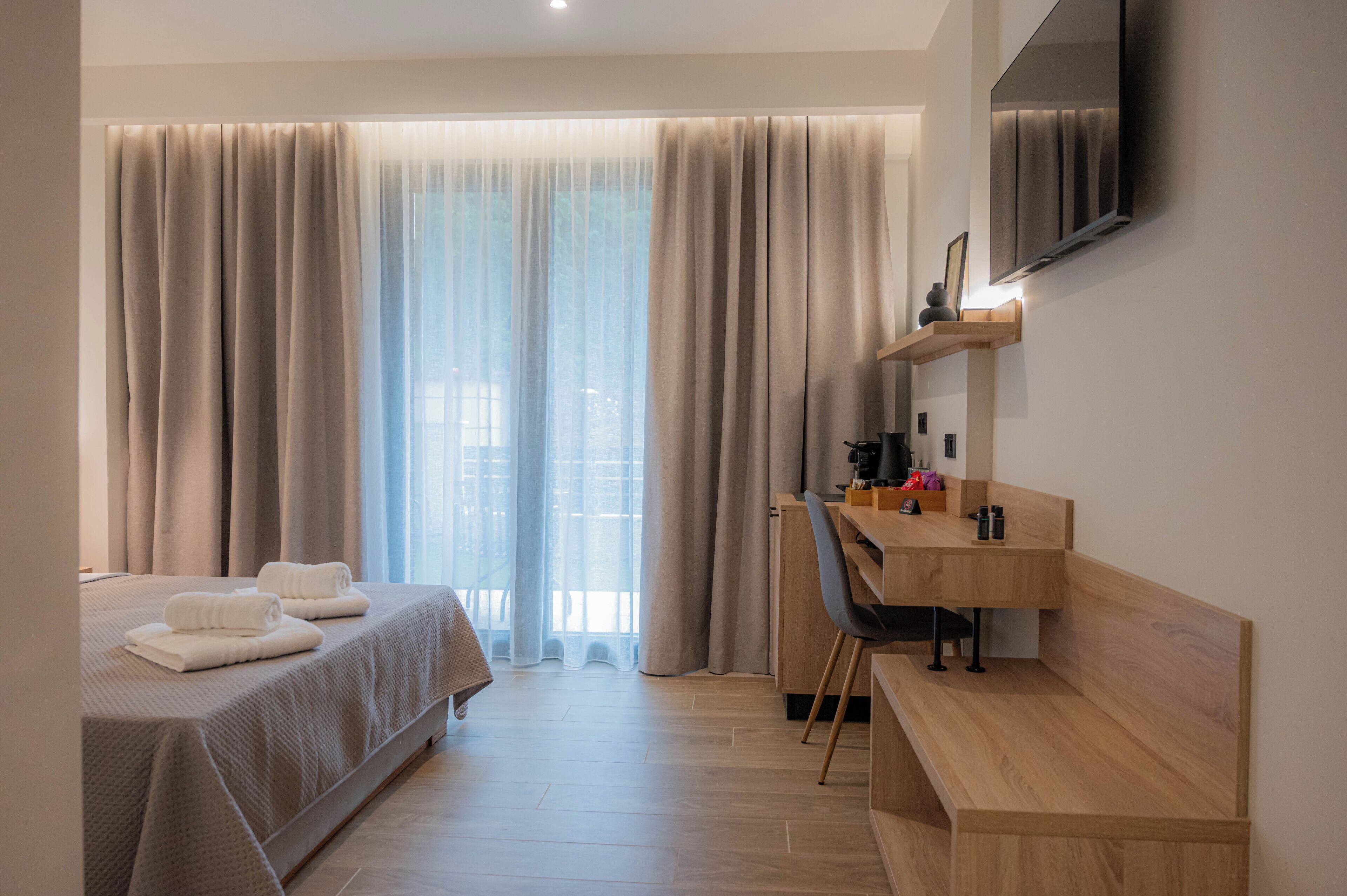Ein Hotelzimmer mit Bett, Schreibtisch, Stuhl, Fernseher und großen Fenstern mit Vorhängen.