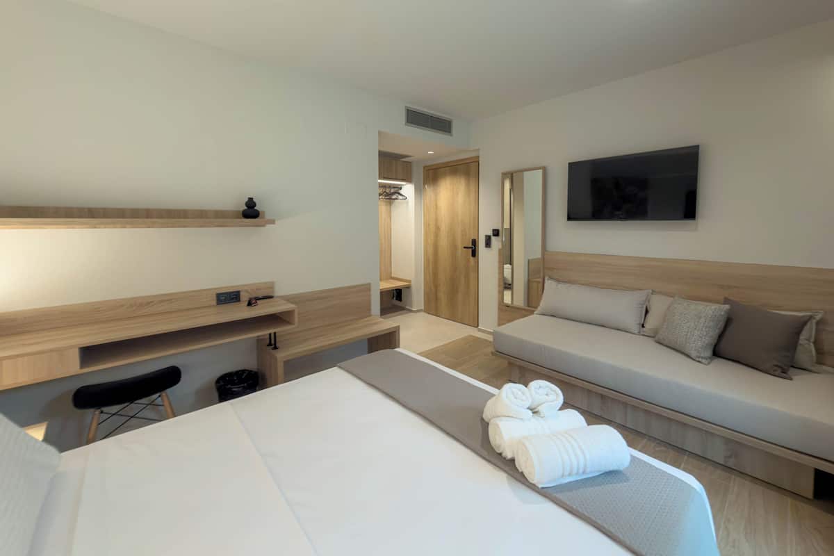 A modern hotel room with a bed, a sofa, a desk, and a mirror.