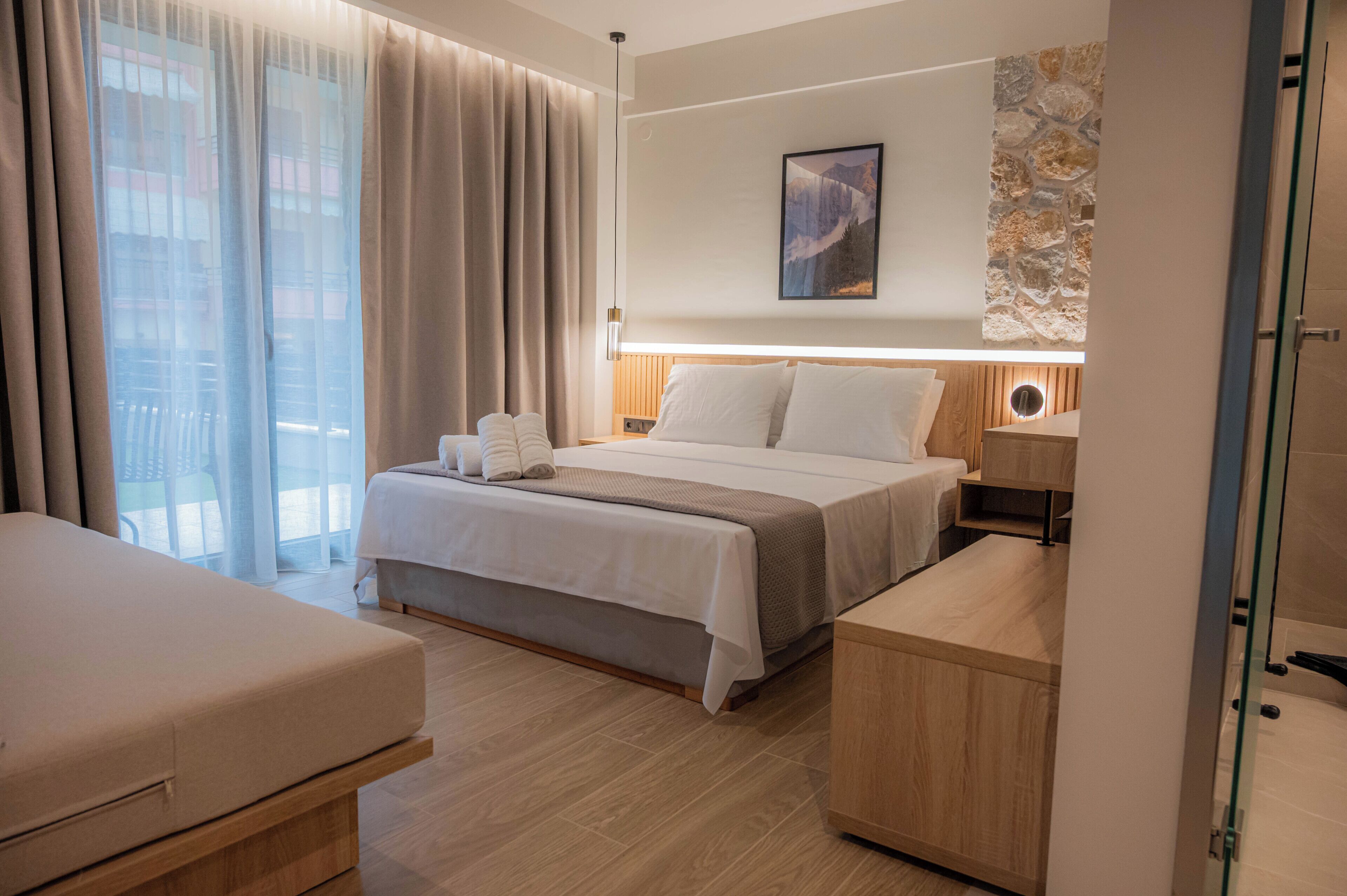Une chambre d’hôtel avec un lit, des tables de chevet, un bureau, une chaise et une grande fenêtre avec des rideaux.