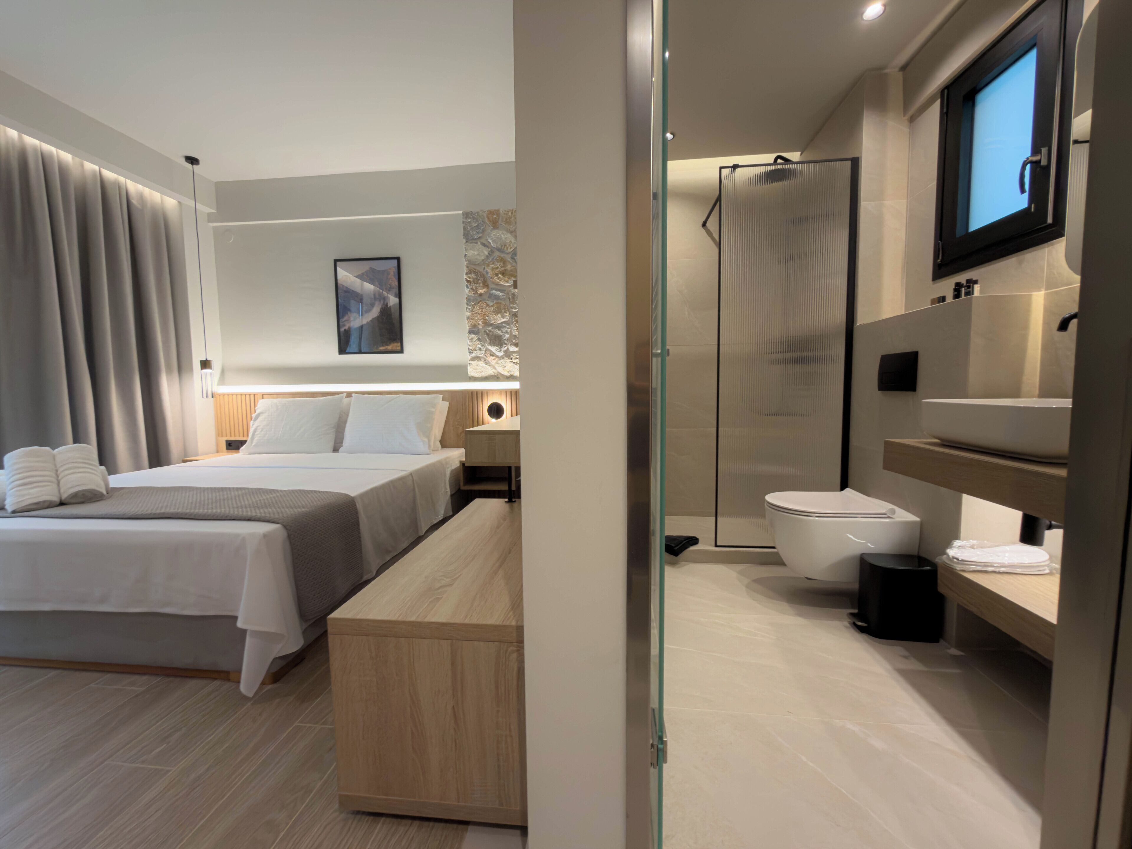 Moderni hotellihuone, jossa on sänky, yöpöytä ja suihkutila.