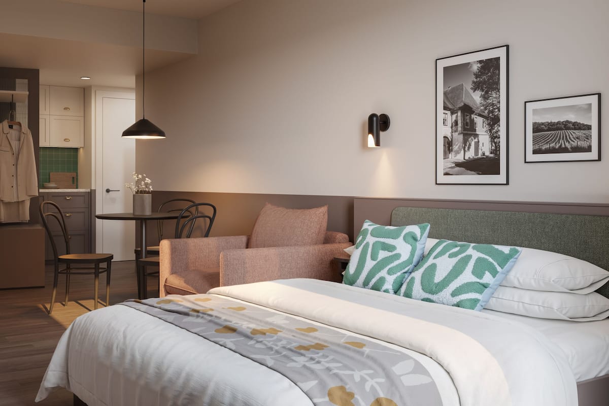 A bedroom with a bed, a chair, a table, and a kitchenette.