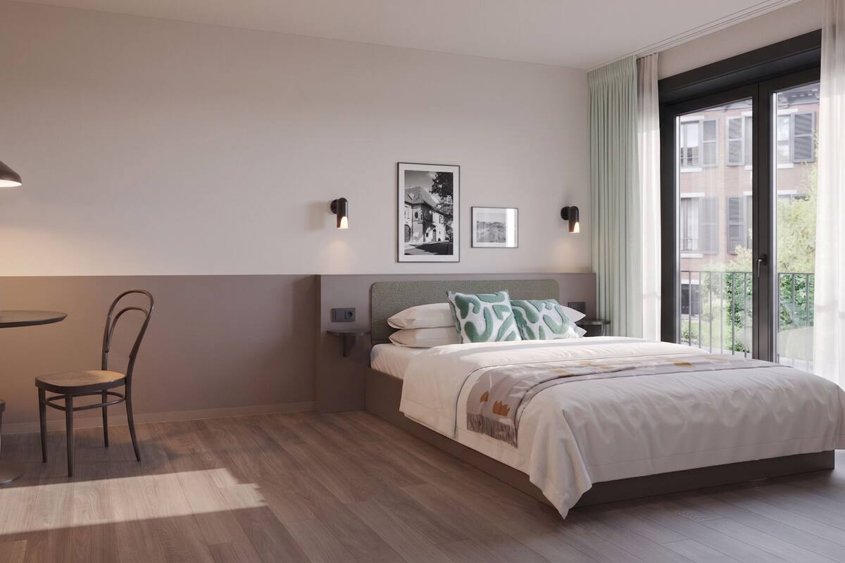 A hotel room with a bed, a table with chairs, a pendant light, and two wall-mounted lights.