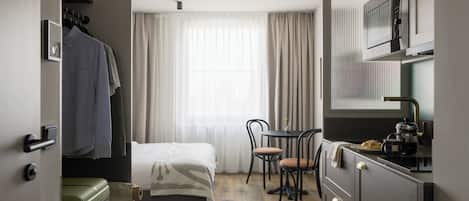 A compact hotel room with a bed, a small dining table, chairs, a kitchenette, and a wardrobe.
