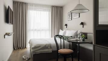 A modern hotel room with a bed, a sofa, a dining table, a chair, a TV, and a window with curtains.