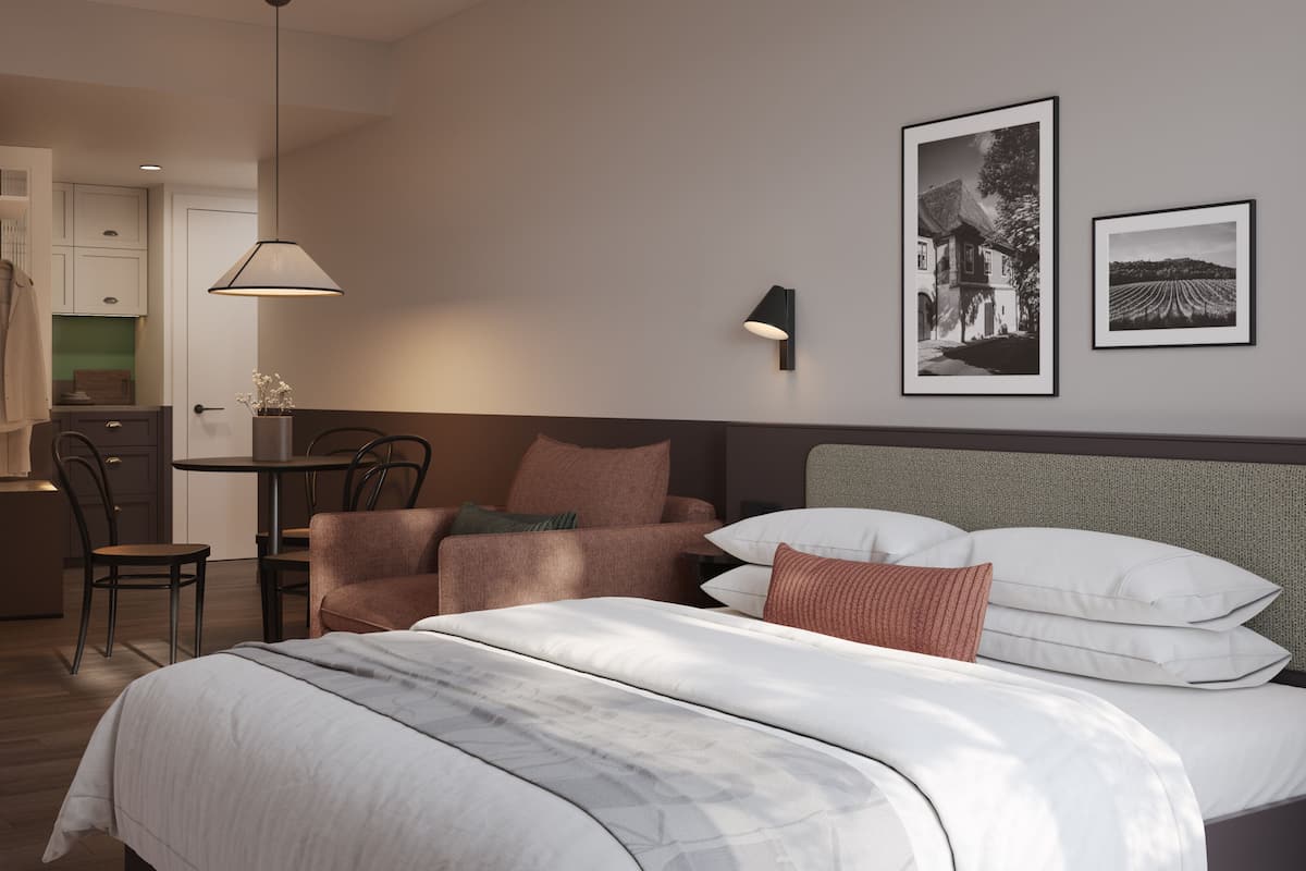 A hotel room with a bed, a chair, a table, and a kitchenette.