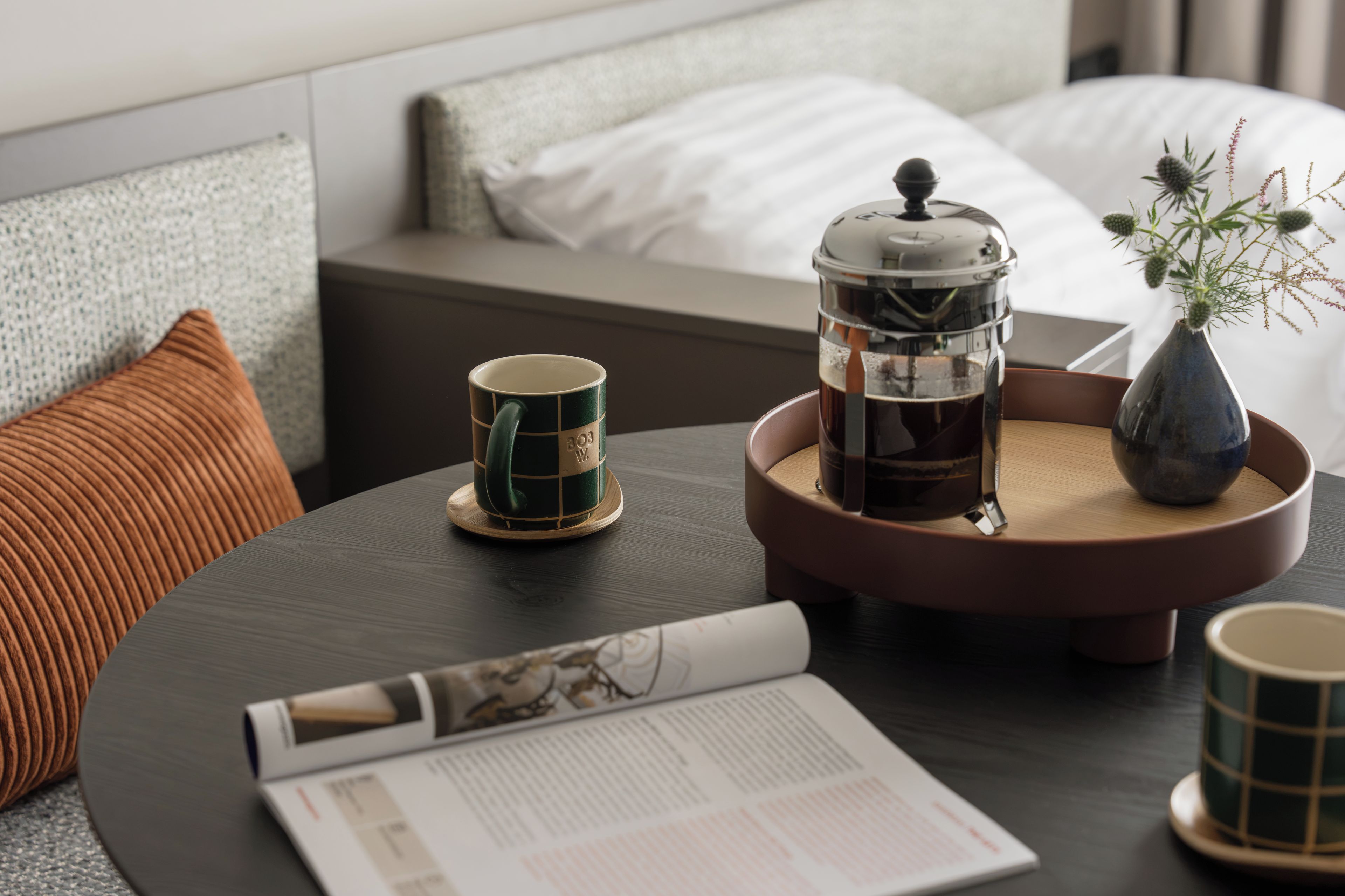 A neatly arranged coffee table with a coffee maker, a mug, a vase with flowers, and a magazine.