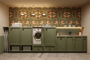 A laundry room with a washing machine, green cabinets, and a patterned wall.