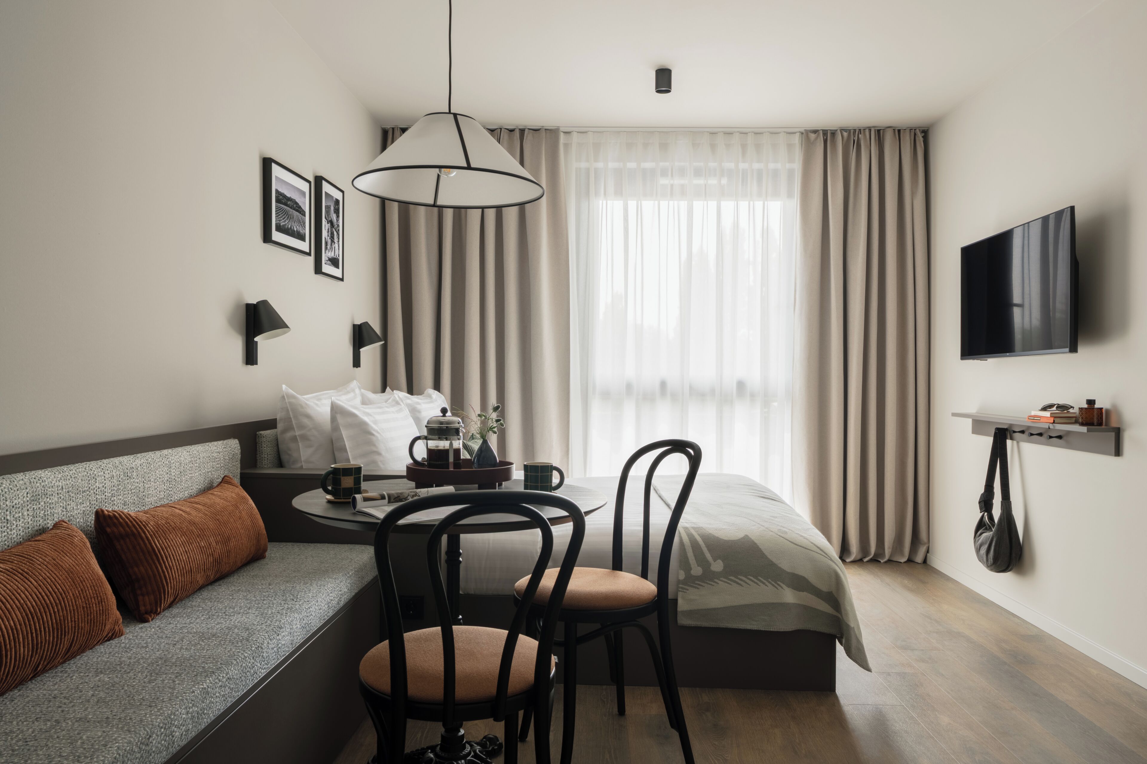 Une chambre d’hôtel moderne équipée d’un canapé, d’une table à manger, de chaises, d’une table basse, d’un téléviseur et d’une fenêtre avec des rideaux.