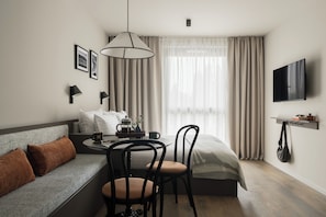 A modern hotel room with a sofa, a dining table, chairs, a coffee table, a TV, and a window with curtains. - Bob W Vienna Döbling (Vienna)