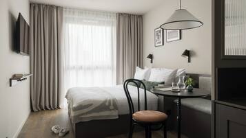 Una habitación de hotel moderna con cama, sofá, mesa de comedor, silla, televisor y ventana con cortinas.