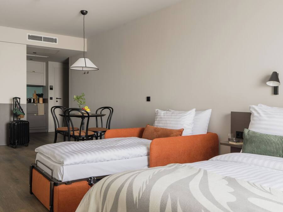 Une chambre d’hôtel avec deux lits, une table à manger, des chaises, un petit coin cuisine et un tableau encadré au mur.