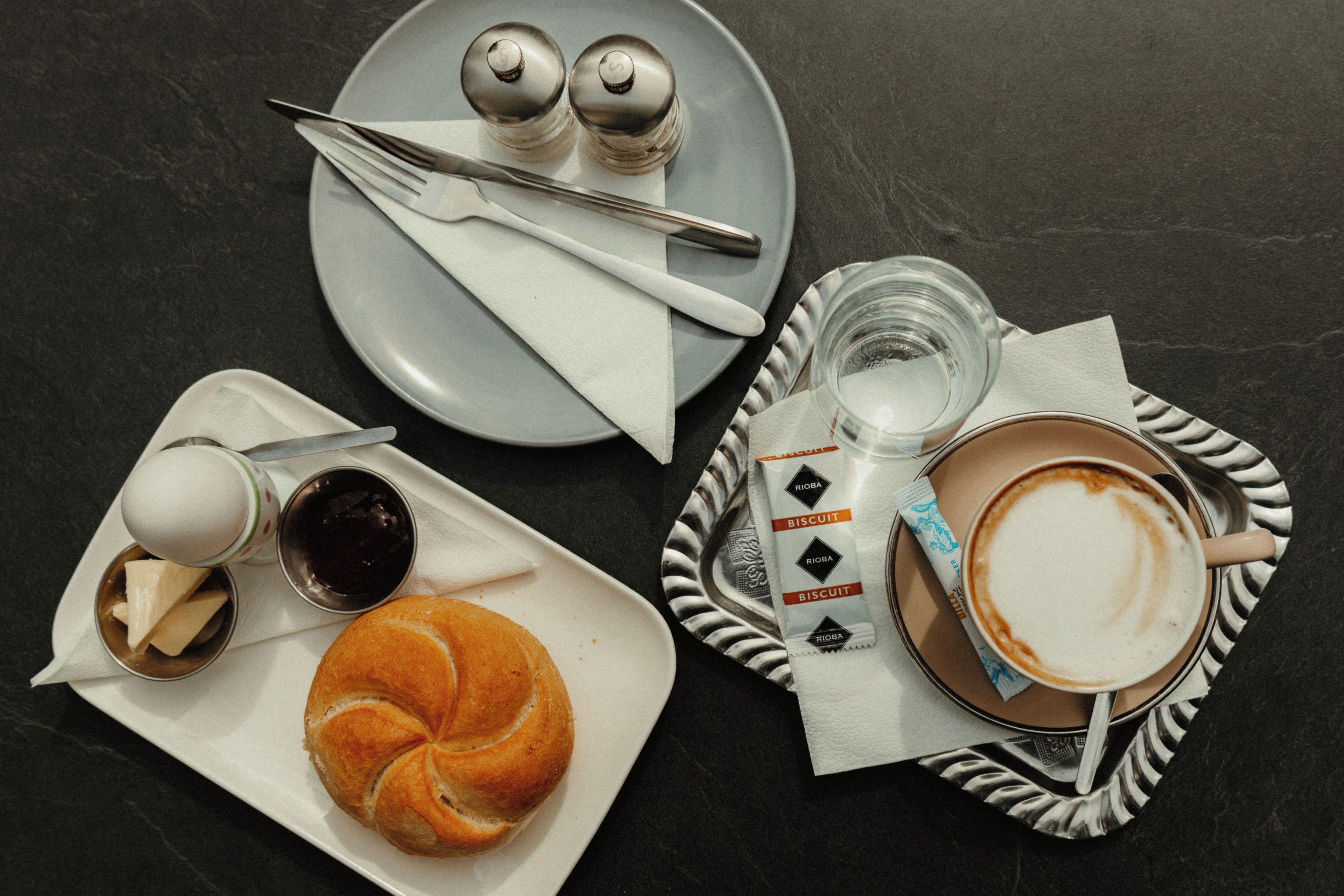 Ein Tisch mit einem Croissant, einer Tasse Kaffee, einem kleinen Marmeladenglas und einer Platte mit Salz- und Pfefferstreuern.