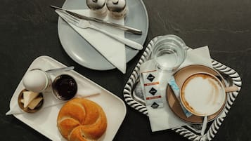 Une table dressée avec un croissant, une tasse de café, un petit pot de confiture et une assiette avec des salières et des poivrières.