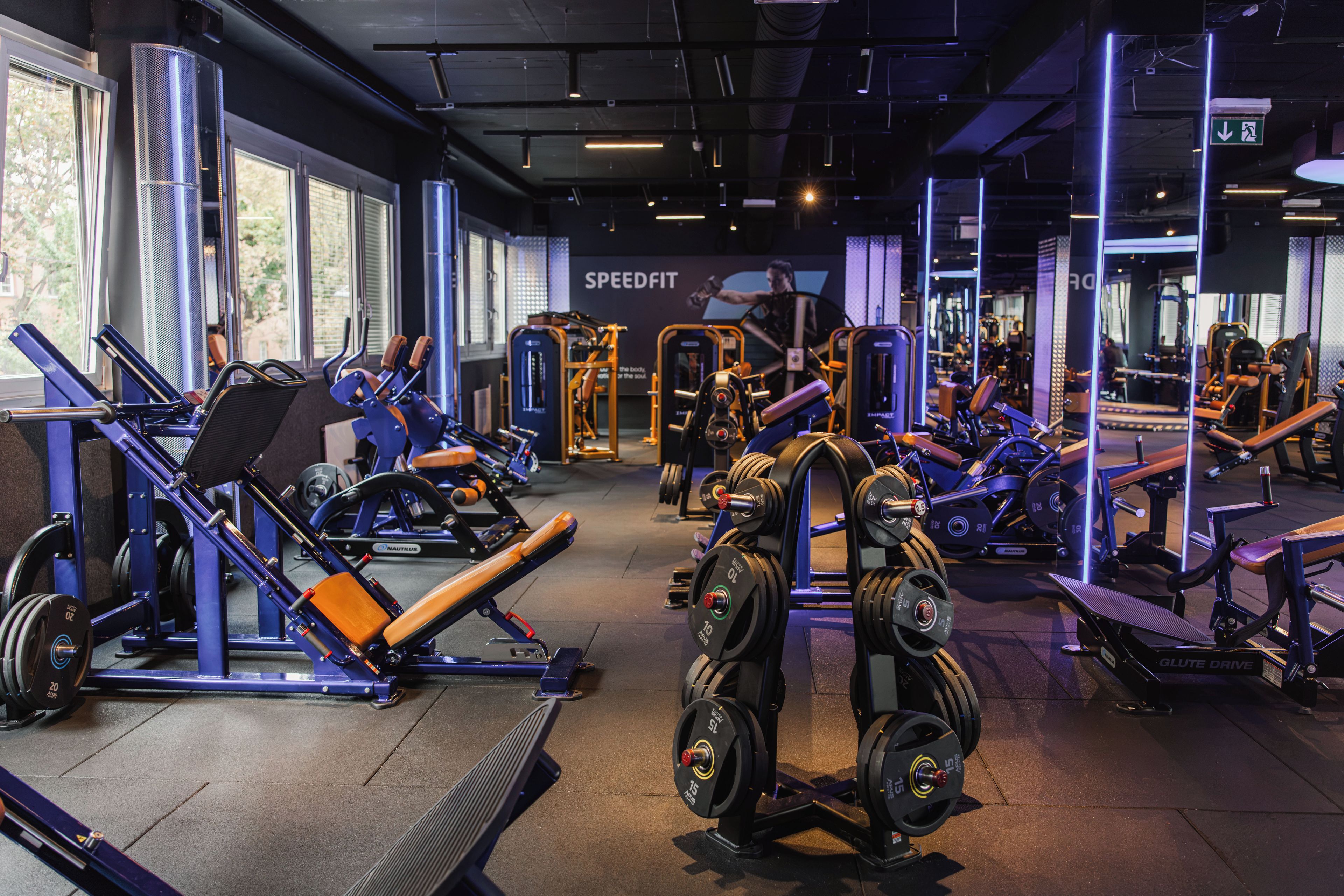 Een sportschool met diverse fitnessapparaten, grote ramen en een bord waarop 'SPEEDFIT' staat.