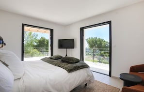 Ein Schlafzimmer mit Bett, Fernseher und Blick auf einen Balkon.