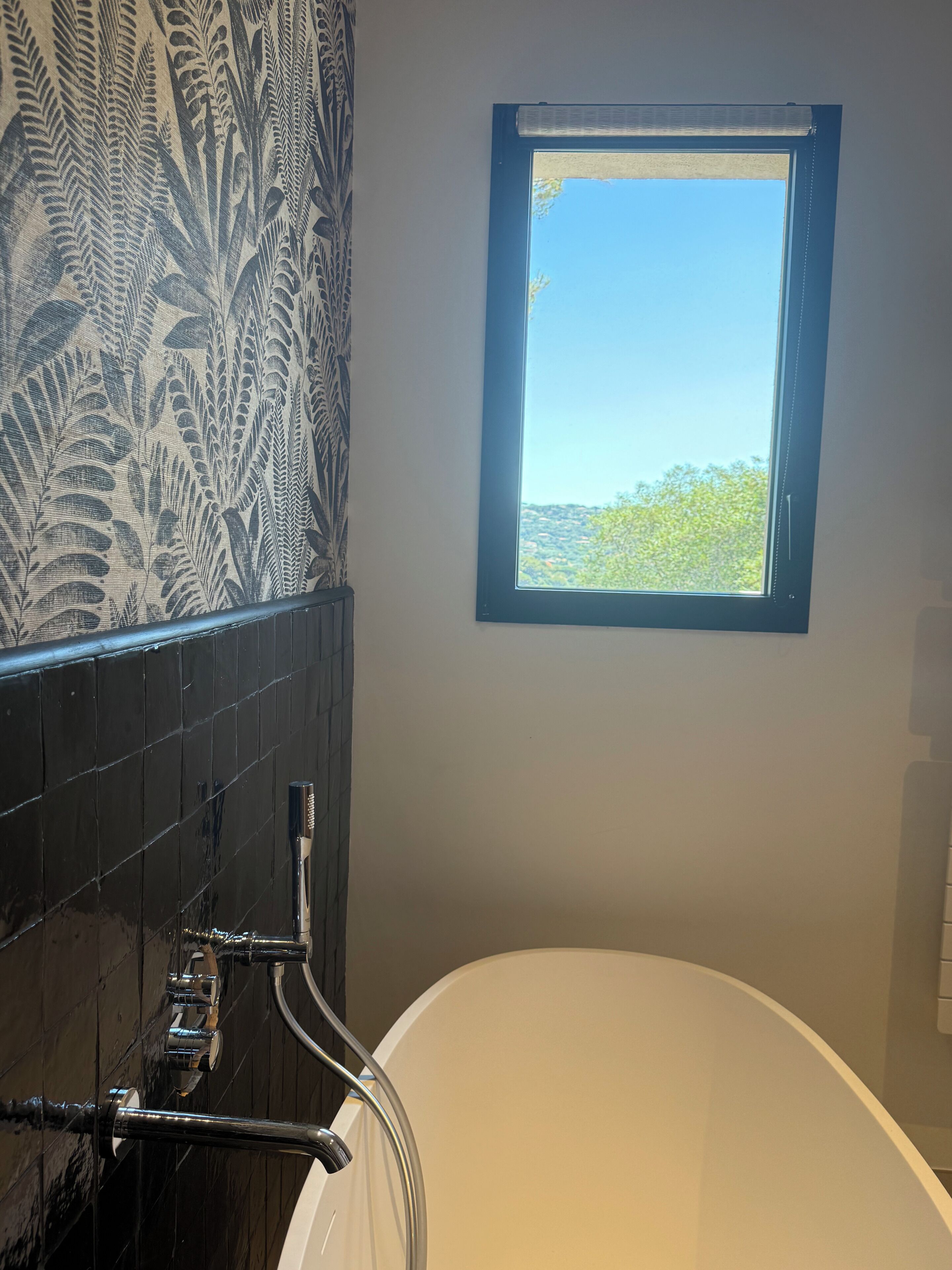 A bathroom with a bathtub, a shower, and a window with a view of greenery.