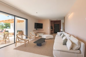 Ein modernes Wohnzimmer mit einer Couch, Sesseln, einem Flachbildfernseher und einem großen Fenster.