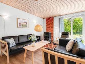 Una sala de estar moderna con un sofá de cuero negro, una mesa de centro de madera, una chimenea y un amplio ventanal con vistas a la vegetación.